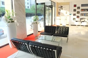 A modern lobby with a glass coffee table, two black leather chairs, and a white reception desk.