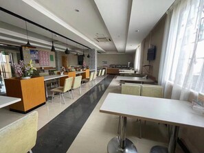 Un comedor moderno con mesas y sillas largas, un mostrador de recepción y una pantalla de televisión en la pared.