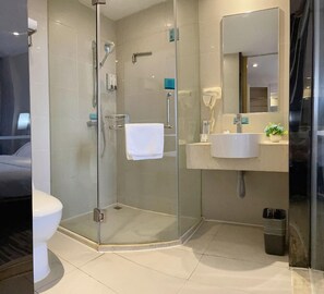 Un baño moderno con ducha envuelta en vidrio, inodoro blanco y lavamanos con espejo.