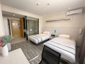 Une chambre d’hôtel avec deux lits, un bureau, une chaise, un espace douche et un appareil de climatisation.