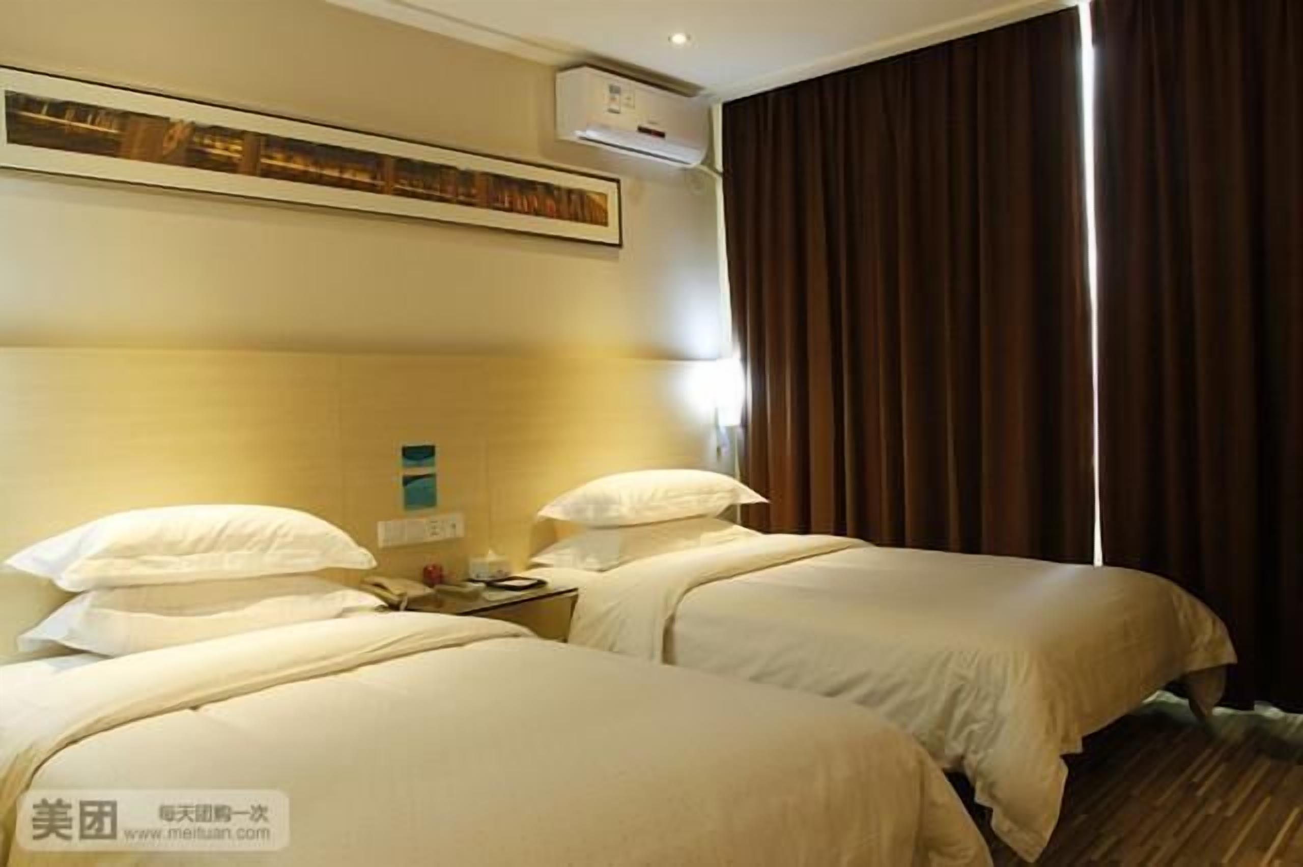 A hotel room with two beds, a nightstand, an air conditioning unit, and a window with curtains.