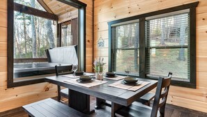 Ein Essbereich aus Holz mit einem Tisch für vier Personen, großen Fenstern und Blick auf Bäume.