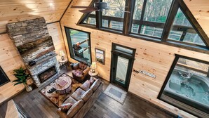 Ein gemütliches Blockhaus-Interieur mit Kamin aus Naturstein, Holzwänden, großen Fenstern und Deckenventilator.