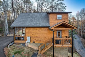A two-story wooden cabin with a stone foundation, a covered porch, and a small deck. - NEW MTN Retreat ~ Prime Location (Sevierville)