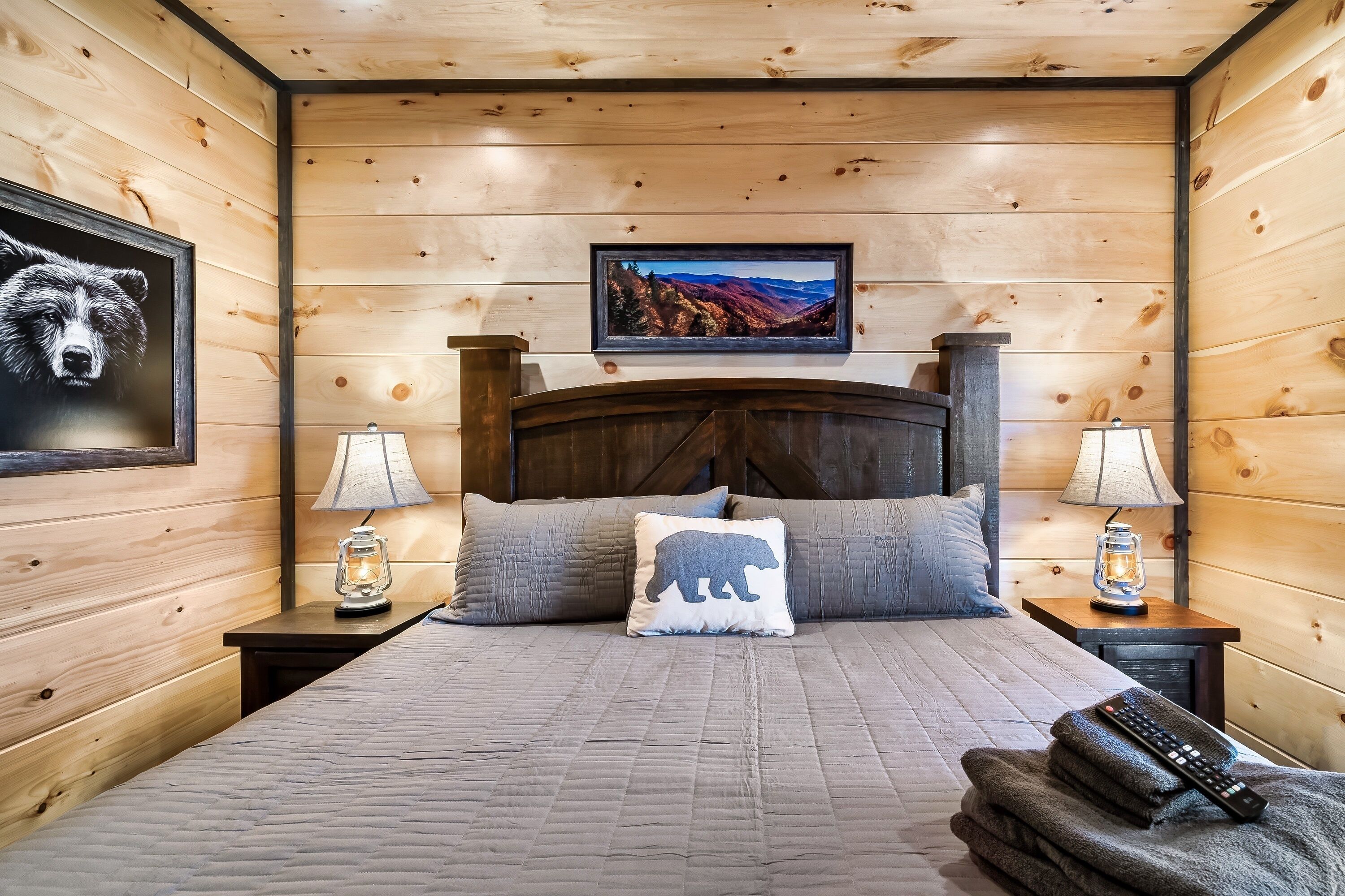 A wooden-paneled room with a bed, two nightstands, a lamp, a framed picture, and a remote control on the bed.