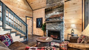 Ein gemütliches Blockhaus-Interieur mit Kamin, Holzwänden, einer Treppe und einer komfortablen Sitzecke.