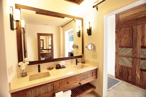 Un baño con un espejo grande, dos lavamanos, tocador de madera y una puerta de madera.