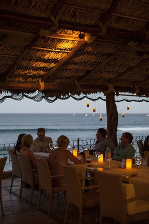 Un restaurante con techo de paja y mesas al aire libre con vistas al océano.