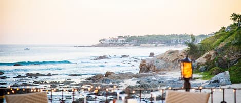Un espace de restauration situé en bord de mer, avec des tables dressées pour les clients, offrant une vue sur l’océan et une côte rocheuse.