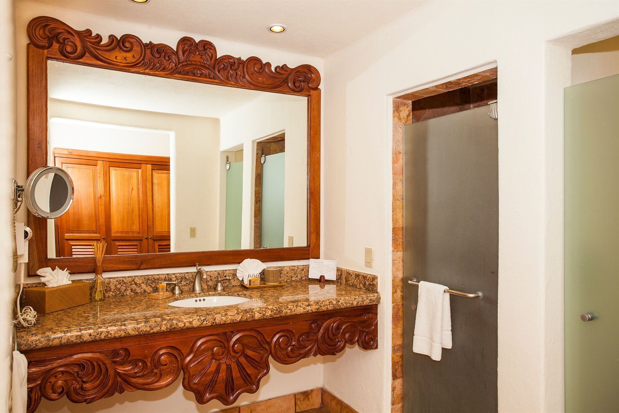 Une salle de bain dotée d’un grand miroir, d’un meuble-lavabo en bois, d’un plan de travail en granit et d’un porte-serviettes.