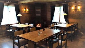 A rustic interior with wooden tables and chairs, a fireplace, and wall-mounted lamps. - Hammarstrand Budget Hotell Vandrarhem - Hostel (Hammarstrand)