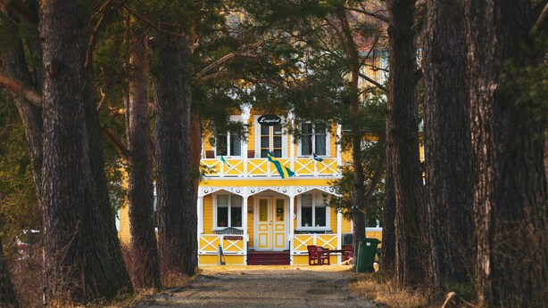 A yellow building with a porch and two doors, surrounded by trees. - Hammarstrand Budget Hotell Vandrarhem - Hostel (Hammarstrand)