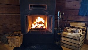 A wood-burning stove with logs, a basket, and a stack of firewood in a log cabin setting. - Hammarstrand Budget Hotell Vandrarhem - Hostel (Hammarstrand)