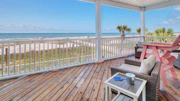 Una terraza de madera con vista a la playa y al océano.