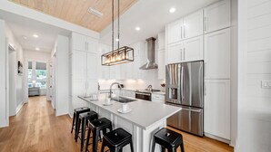 A modern kitchen with white cabinetry, stainless steel appliances, a central island with bar stools, and a wooden ceiling. - One Too Many: 5BR Home on SGI- Beach Views, Priv. Pool, Sleeps 14 (St. George Island)