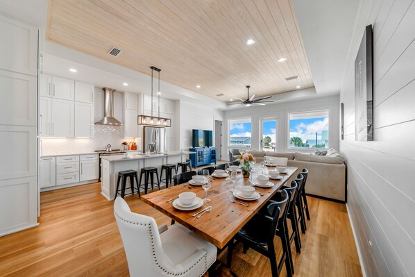 A modern kitchen with white cabinetry, a wooden dining table set for six, and a large island with bar stools.