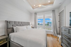 A bedroom with a large bed, a wooden ceiling, a window with curtains, and a dresser.