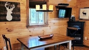 A wooden cabin interior with a wooden table, two chairs, a bench, a fireplace, a television, and wall-mounted candles. - Modern, Private Cabin 20 Minutes From Penn State, Breakfast Items Included (Philipsburg)