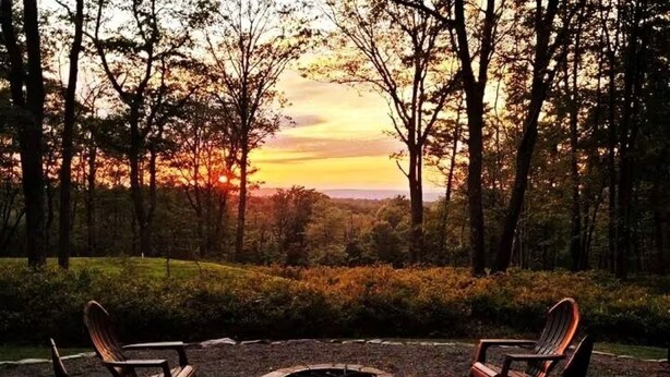 A forested area with two Adirondack chairs facing a fire pit. - Modern, Private Cabin 20 Minutes From Penn State, Breakfast Items Included (Philipsburg)