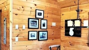A wooden cabin interior with framed pictures on the wall, a wooden bench, and a shelf with candles. - Modern, Private Cabin 20 Minutes From Penn State, Breakfast Items Included (Philipsburg)