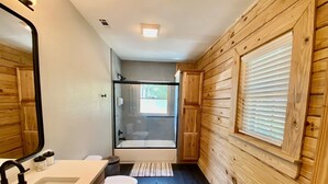 Et badeværelse med trævæg, hvid vask, toilet, badekar og brusebad.