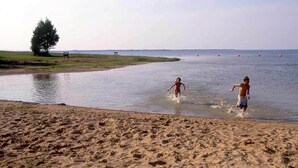 En sandstrand med to personer i vandet.