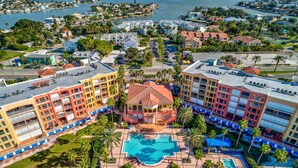 A resort with a central swimming pool, multiple buildings, and a marina in the background.