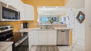 A modern kitchen with white cabinets, stainless steel appliances, and a view of the ocean through large windows.
