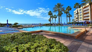 A pool area with lounge chairs and palm trees, surrounded by a building with balconies.