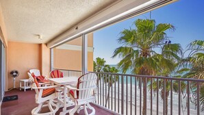 A balcony with white chairs and a table, overlooking a beach with palm trees and the ocean.