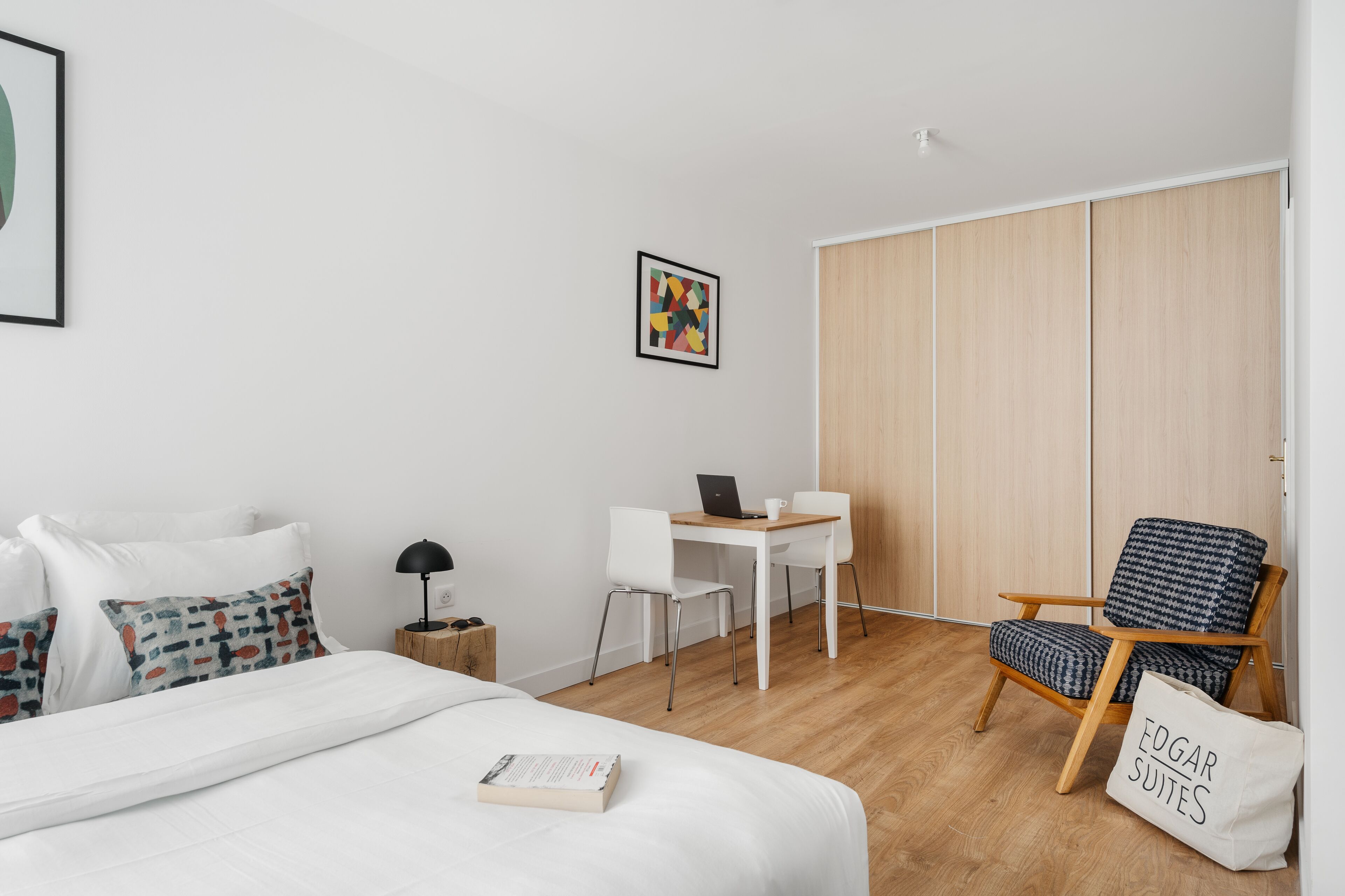 A modern hotel room with a bed, a desk, a chair, and a wardrobe.