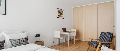 A modern hotel room with a bed, a desk, a chair, and a wardrobe.