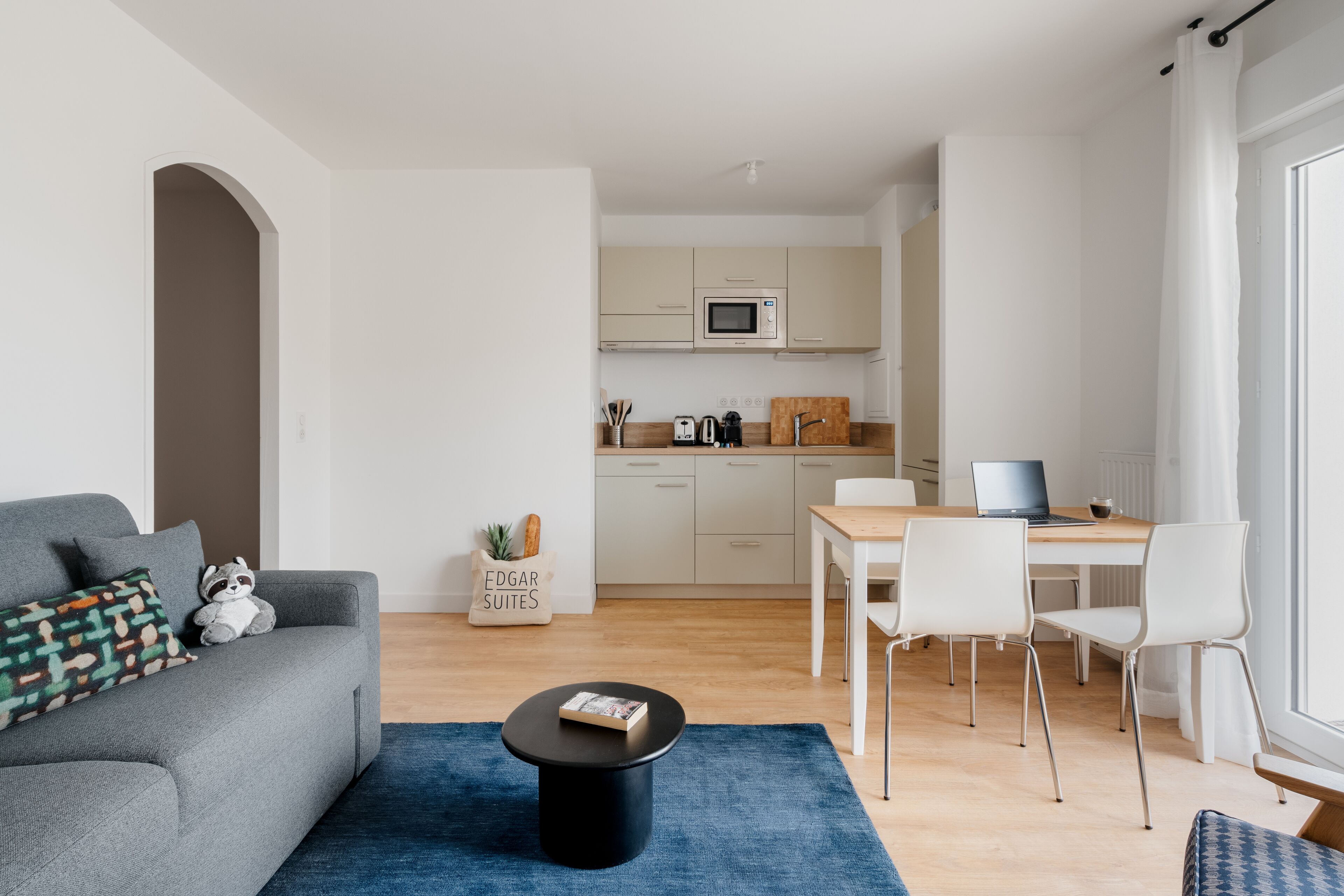 A modern living room with a grey sofa, a black coffee table, and a dining area with a wooden table and white chairs.