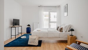 A modern hotel room with a bed, a desk with a TV, a suitcase, and a bag labeled "Edgar Suites". - Edgar Suites Meudon-La-Forêt (Meudon)