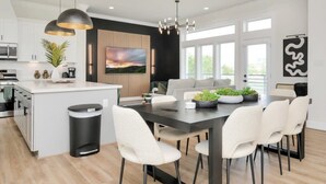 A modern kitchen with a central island, white cabinetry, and a dining area with a dark table and white chairs. - Paradise Palace Best Rooftop in HTX w/ Hot Tub (Houston)