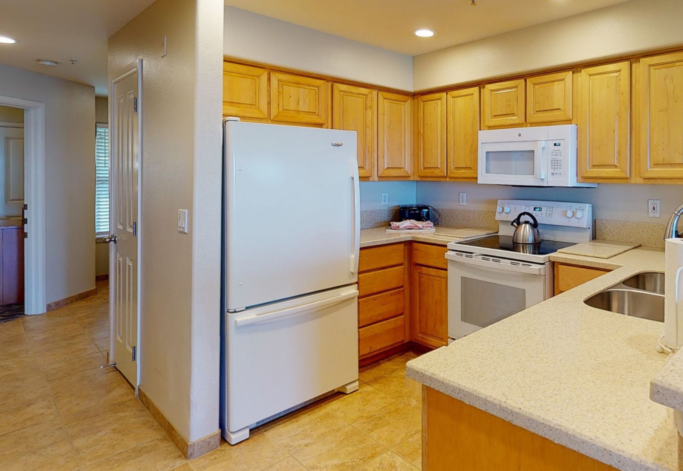 A kitchen with wooden cabinets, a refrigerator, a microwave, an oven, and a sink.