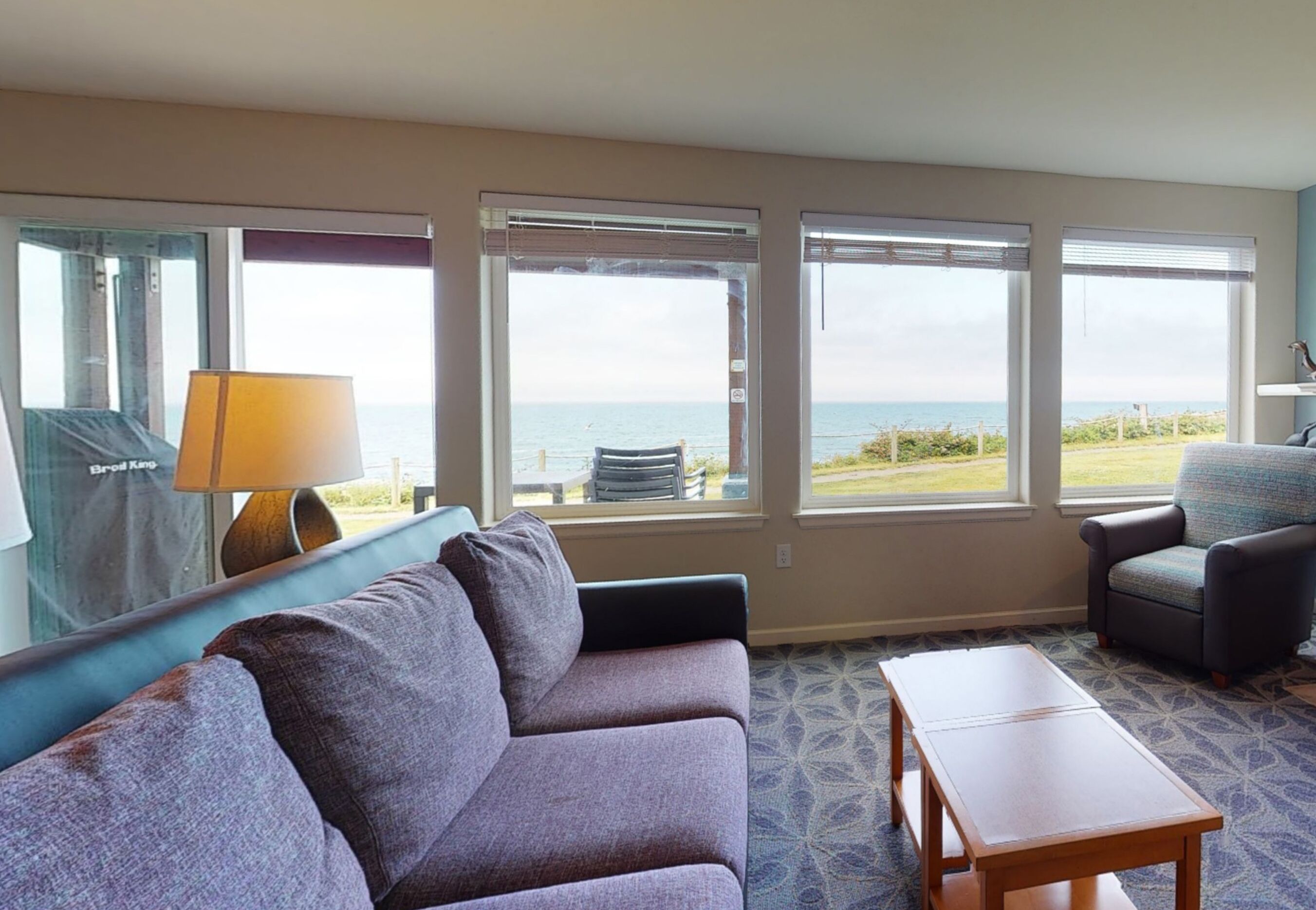 A hotel room with a large window offering a view of the sea, a sofa, a chair, and a small table.