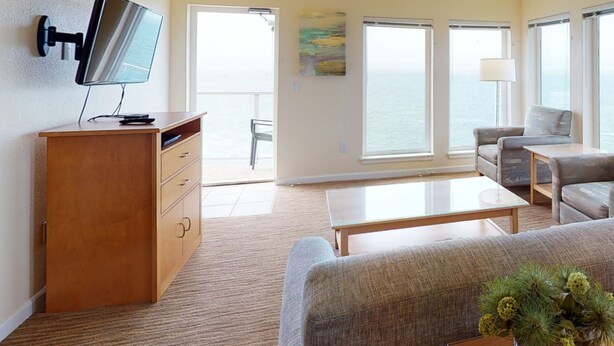 Ein modernes Wohnzimmer mit Flachbildfernseher, einer Holzkommode, einem Sofa, einem Couchtisch und großen Fenstern mit Meerblick.