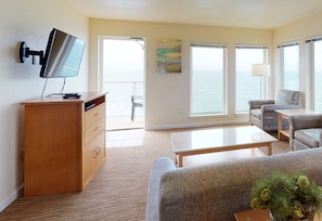 A modern living room with a flat-screen TV, a wooden cabinet, a sofa, a coffee table, and large windows offering a view of the sea. - Whale Pointe - Ocean Front 3bd3ba - Assignment 1 (Depoe Bay)