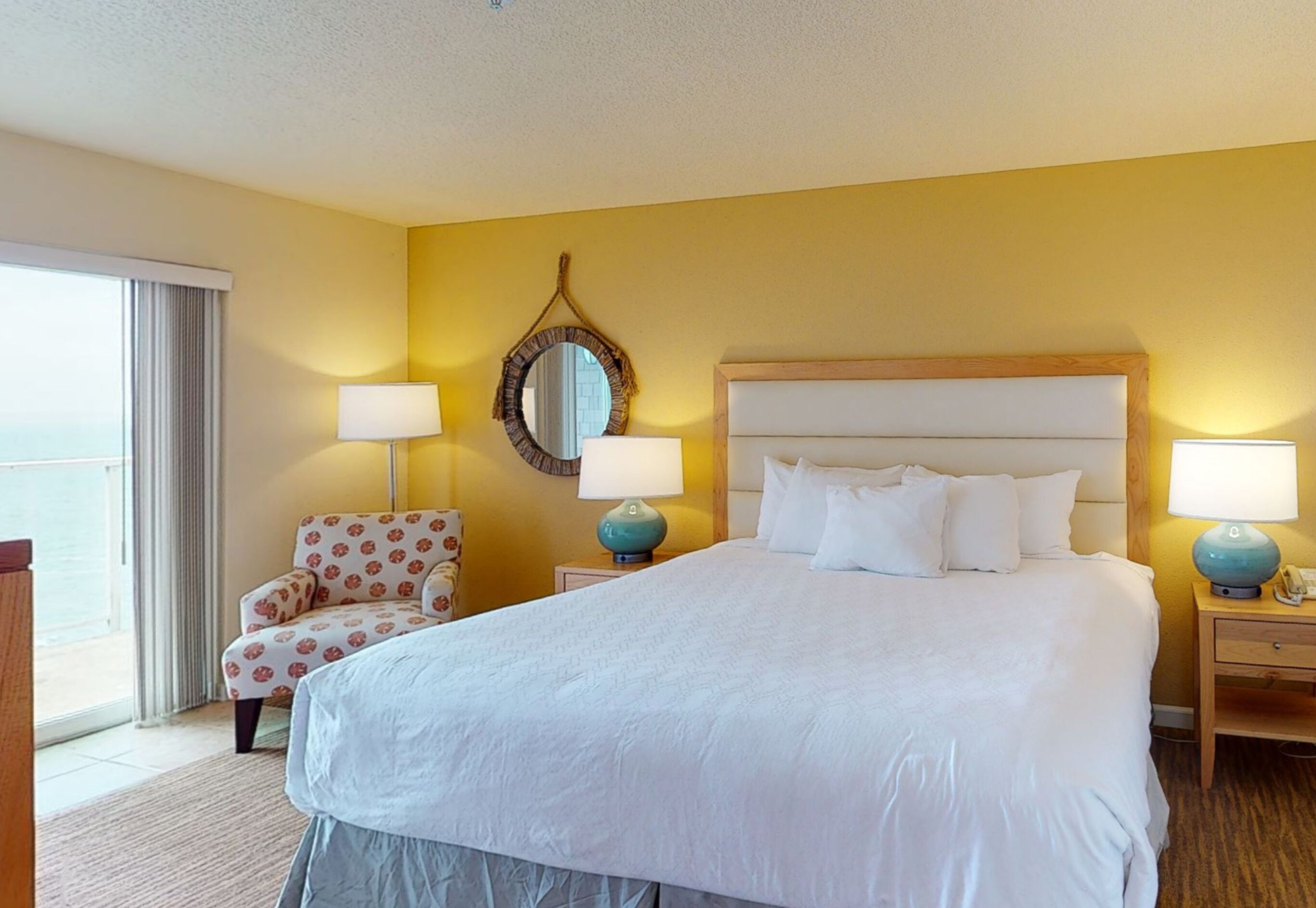 A hotel room with a large bed, two bedside tables with lamps, a chair, a mirror, and a view of the outside.