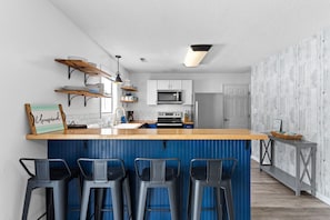 Uma cozinha moderna com área de bar, armários brancos, micro-ondas e uma parede com detalhes em azul.