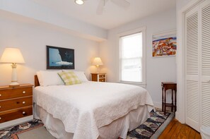 A bedroom with a bed, two bedside tables, a nightstand, a window, and a door.