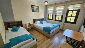 Habitación de hotel con dos camas, un escritorio y una silla. Cuenta con ventanas con persianas, un radiador y un cuadro en la pared.