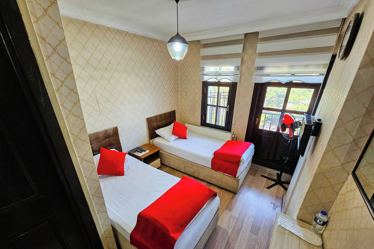A hotel room with two beds, a ceiling fan, a window with a view, and a door.
