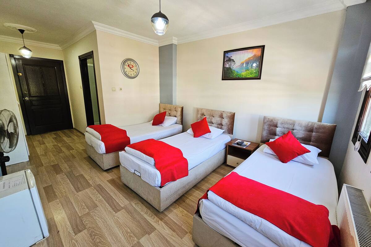 A hotel room with three beds, a clock, a painting, and a fan.