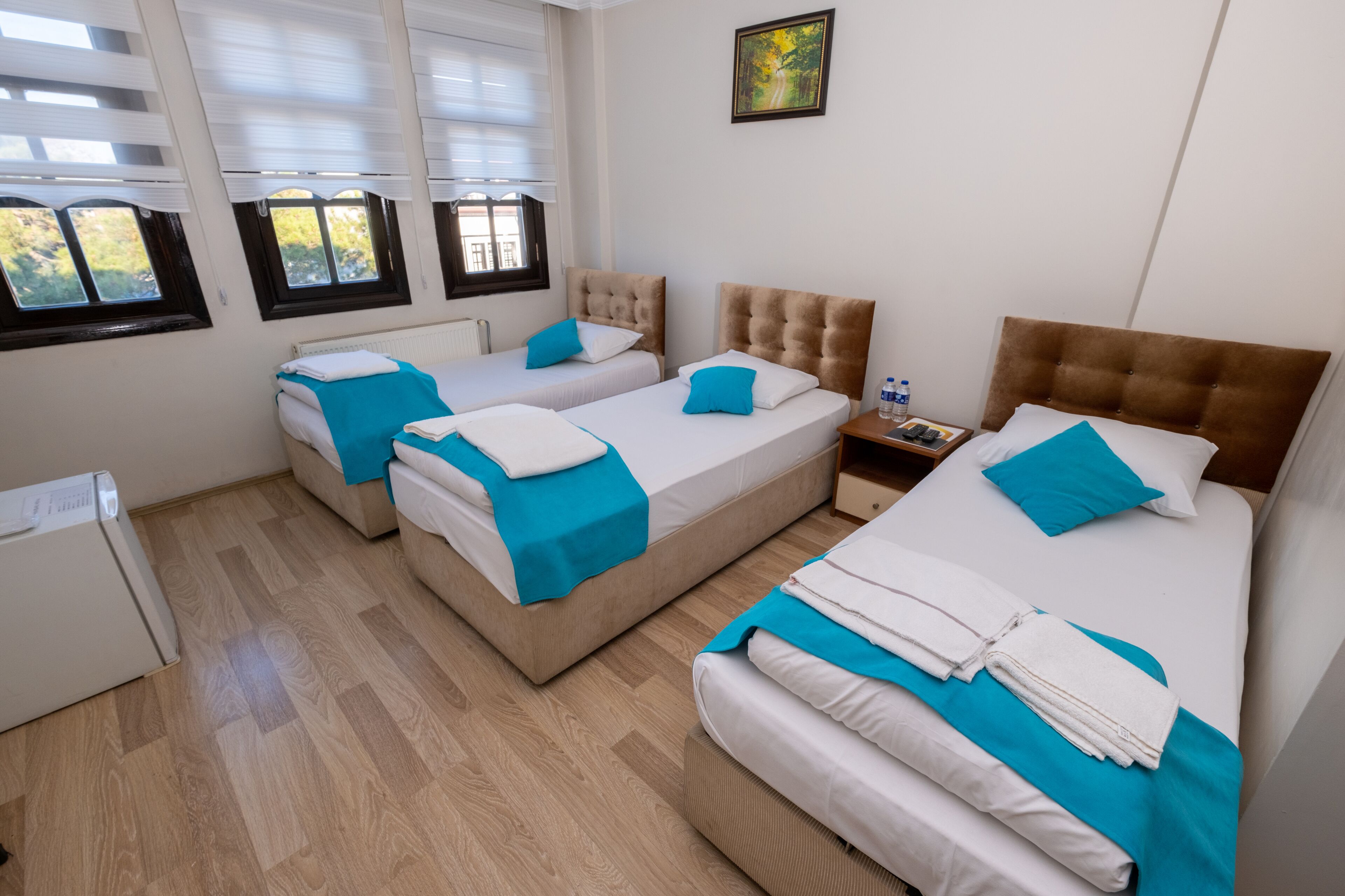 A hotel room with two single beds, a large bed, and a small table with a water bottle.