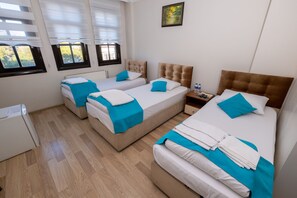 Ein Hotelzimmer mit zwei Einzelbetten, einem großen Bett und einem kleinen Tisch mit einer Wasserflasche.