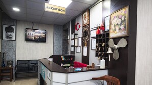 Un área de recepción con mostrador, televisor, certificados enmarcados, un reloj y un ventilador fijado a la pared.