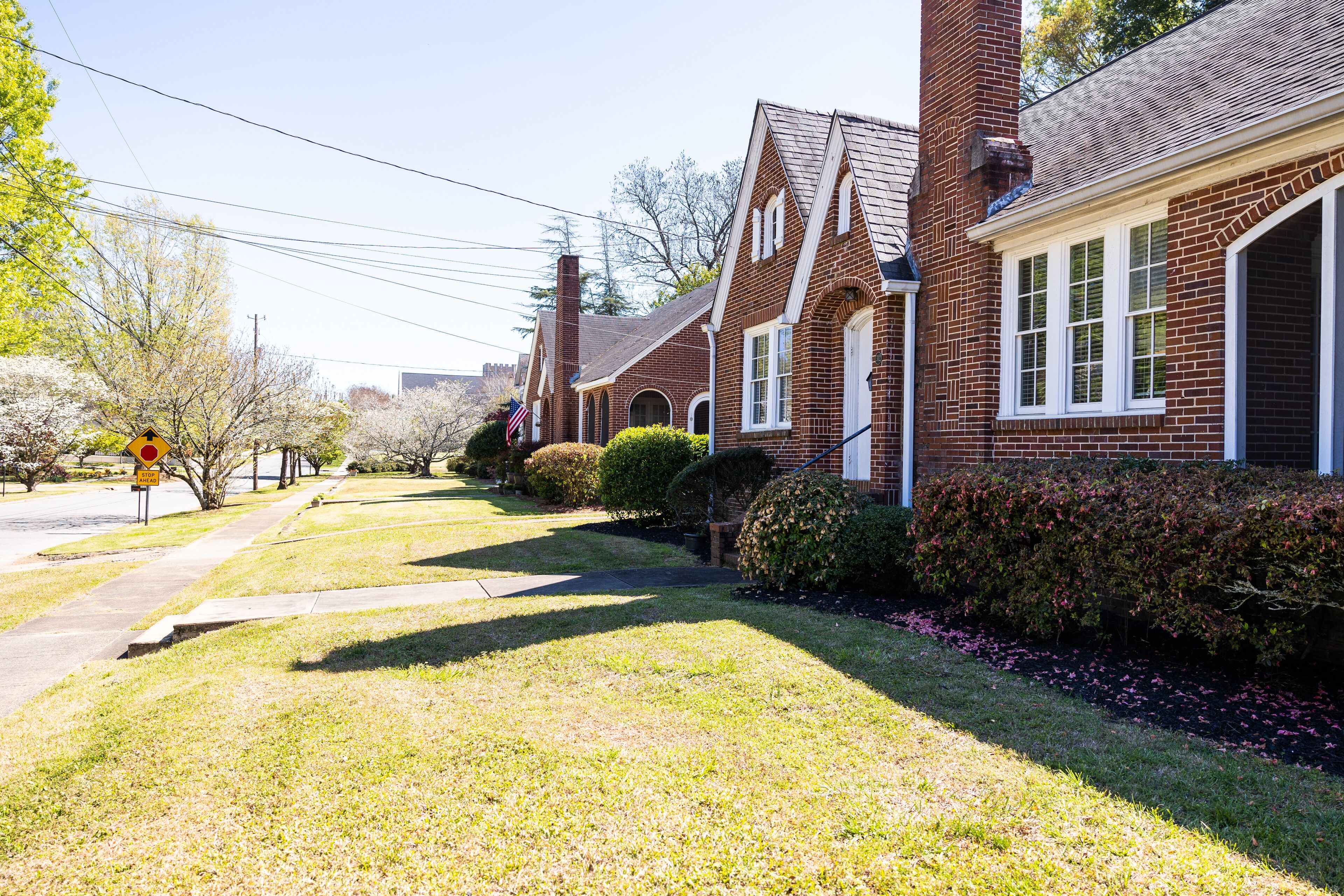 A row of brick houses with a well-maintained lawn and a pedestrian crossing.
