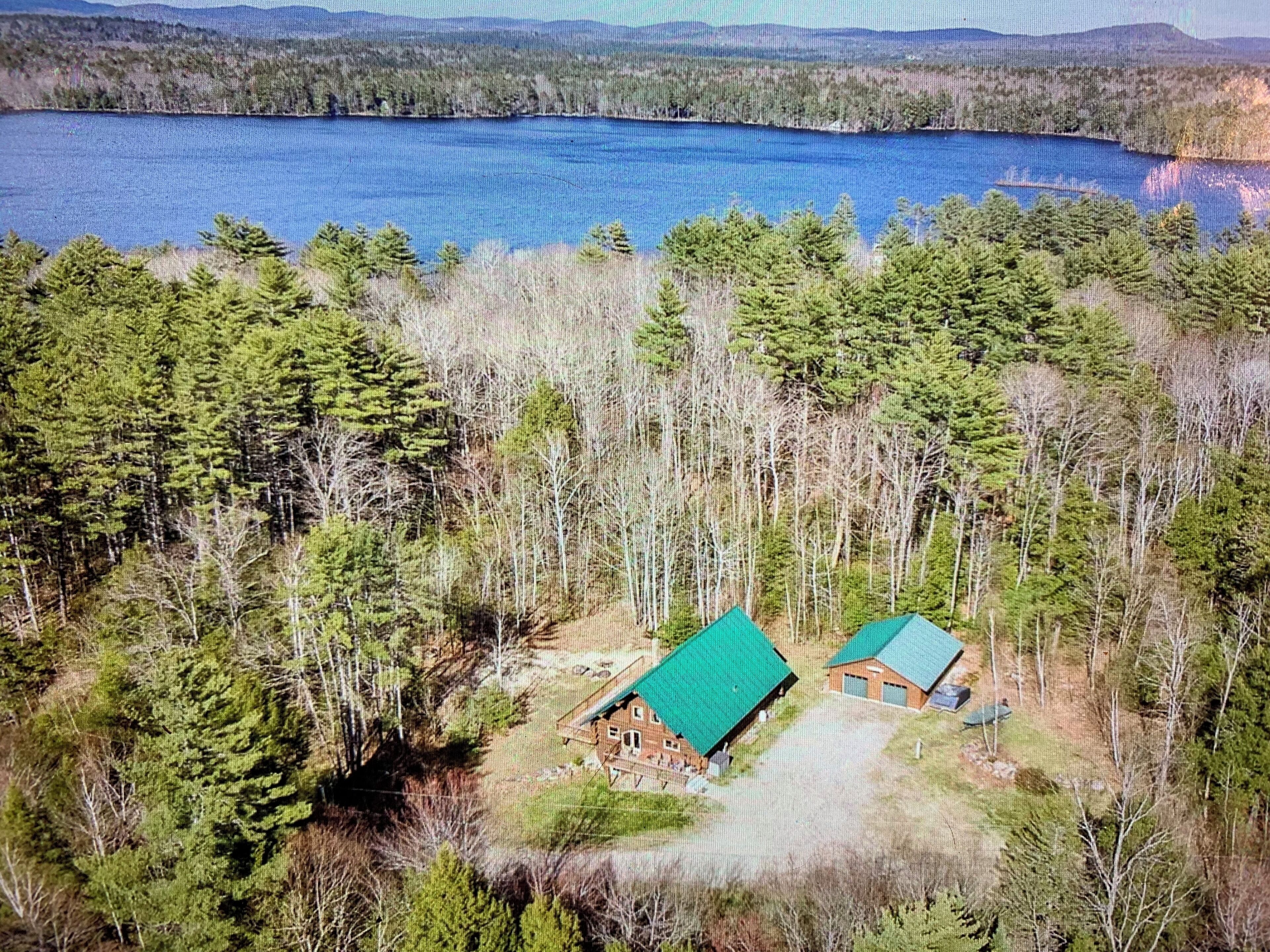 A cabin with a green roof surrounded by dense forest and a lake.